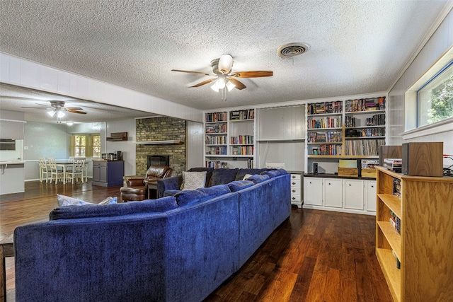 living room featuring a textured ceiling, dark wood-type flooring, a fireplace, and ceiling fan