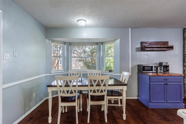 dining area featuring a textured ceiling, wooden walls, and dark hardwood / wood-style floors