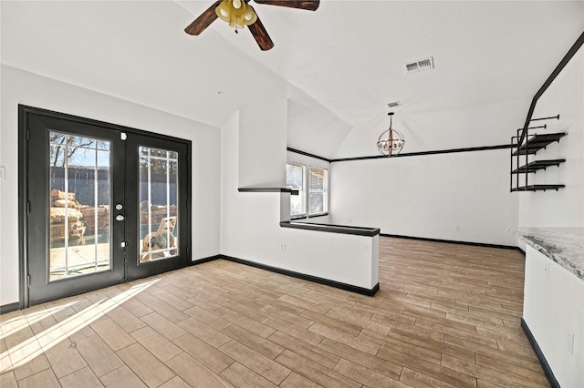 unfurnished living room featuring french doors, plenty of natural light, ceiling fan with notable chandelier, and vaulted ceiling