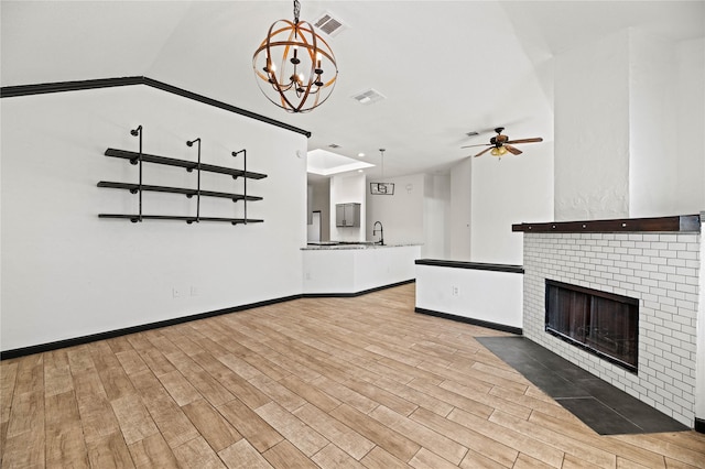 unfurnished living room featuring a fireplace, light wood-type flooring, ceiling fan with notable chandelier, and sink