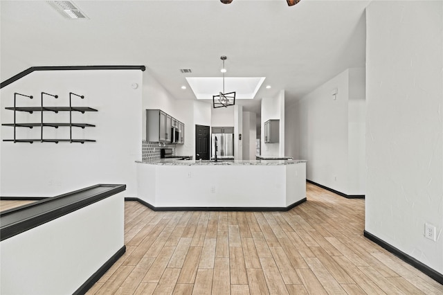 kitchen featuring light stone countertops, stainless steel appliances, an inviting chandelier, kitchen peninsula, and a tray ceiling