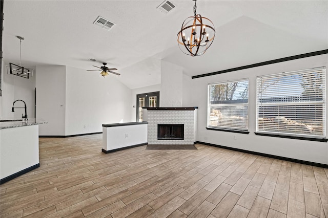 unfurnished living room featuring ceiling fan with notable chandelier, a brick fireplace, lofted ceiling, and sink