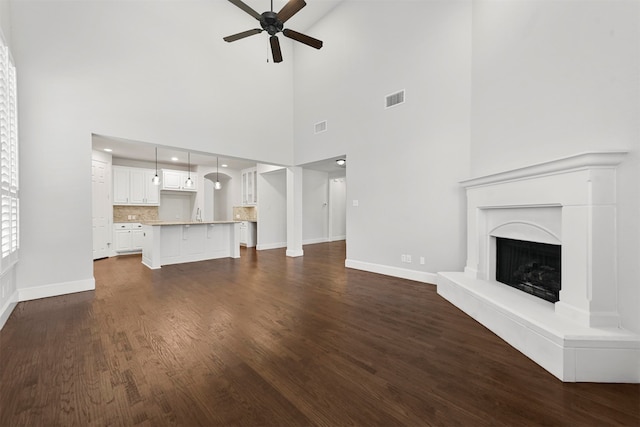 unfurnished living room featuring dark wood-type flooring, a towering ceiling, and ceiling fan