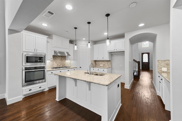 kitchen with dark wood-type flooring, an island with sink, stainless steel appliances, white cabinetry, and light stone counters