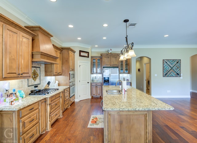 kitchen with a large island with sink, appliances with stainless steel finishes, premium range hood, dark wood-type flooring, and sink