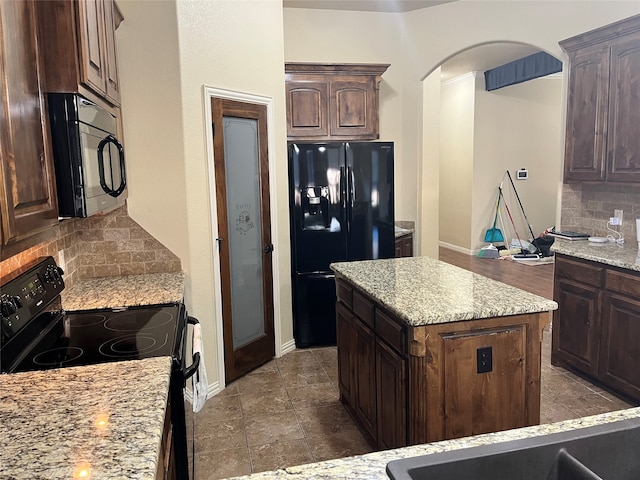 kitchen with black appliances, a kitchen island, dark brown cabinets, light stone counters, and decorative backsplash