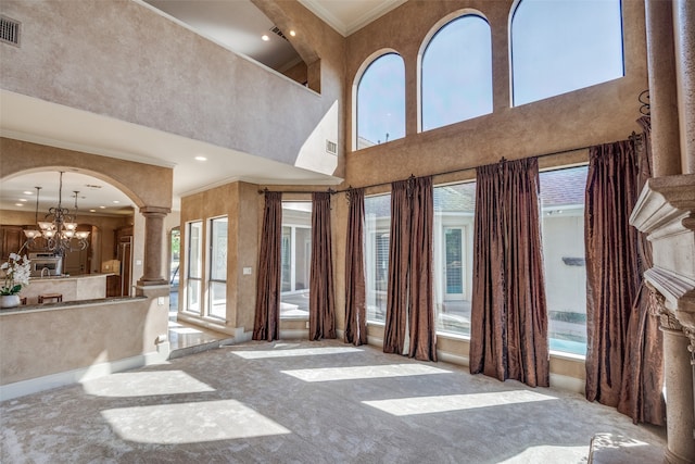 carpeted living room with crown molding, a chandelier, a high ceiling, and decorative columns