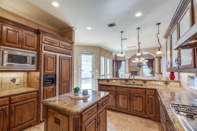 kitchen featuring sink, built in appliances, ornate columns, decorative light fixtures, and a center island