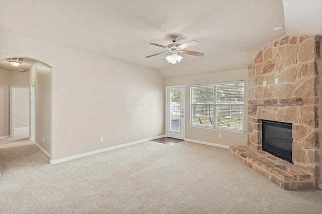 unfurnished living room with carpet, a stone fireplace, ceiling fan, and lofted ceiling