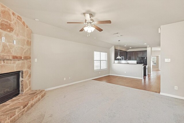 unfurnished living room featuring carpet, sink, vaulted ceiling, ceiling fan, and a fireplace