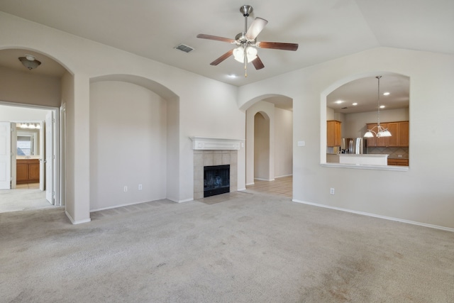 unfurnished living room featuring lofted ceiling, light colored carpet, a tile fireplace, and ceiling fan with notable chandelier