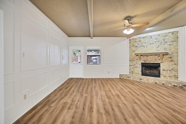 unfurnished living room with hardwood / wood-style floors, a fireplace, vaulted ceiling with beams, ceiling fan, and a textured ceiling