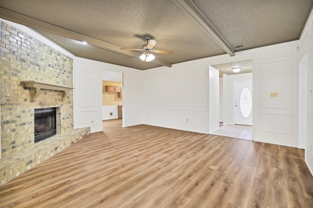 unfurnished living room with ceiling fan, a fireplace, light hardwood / wood-style floors, a textured ceiling, and beamed ceiling