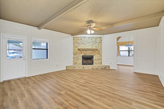 unfurnished living room featuring a brick fireplace, light hardwood / wood-style floors, a textured ceiling, and ceiling fan