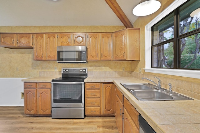 kitchen with stainless steel appliances, tile counters, sink, and light wood-type flooring