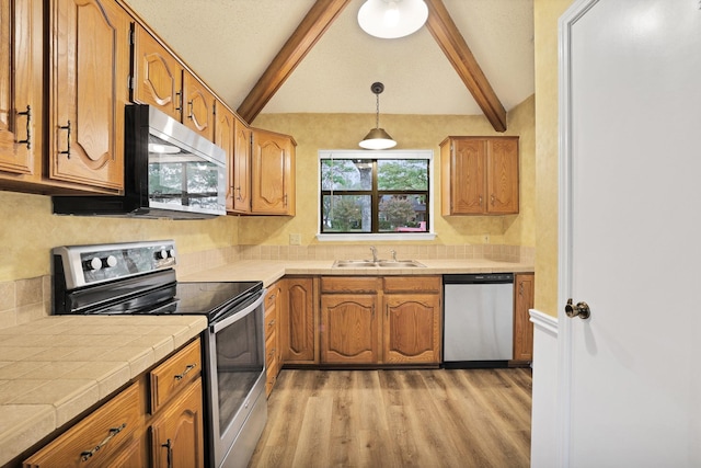 kitchen featuring sink, vaulted ceiling with beams, light wood-type flooring, pendant lighting, and stainless steel appliances