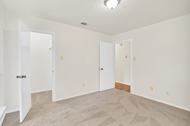 unfurnished bedroom featuring a spacious closet, light carpet, a textured ceiling, and a closet