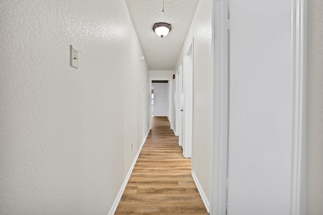 hallway with light hardwood / wood-style floors and a textured ceiling