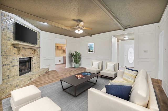 living room featuring hardwood / wood-style floors, a fireplace, beamed ceiling, ceiling fan, and a textured ceiling