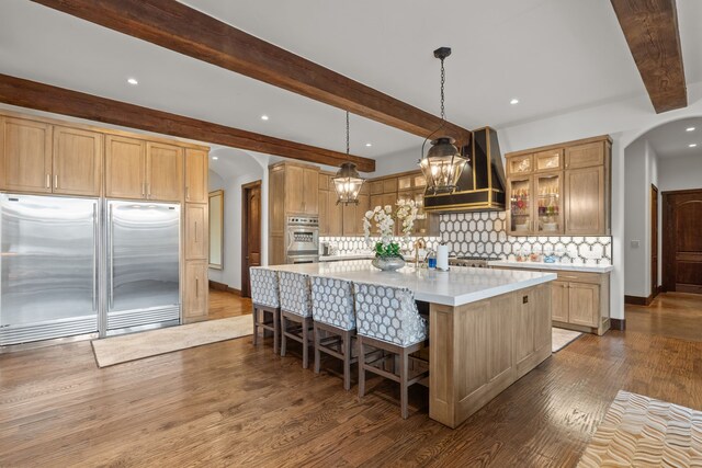 kitchen featuring custom range hood, decorative backsplash, dark hardwood / wood-style floors, and a kitchen island with sink