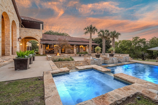 pool at dusk featuring an in ground hot tub and a patio area