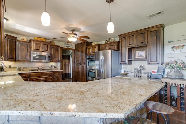 kitchen featuring kitchen peninsula, hanging light fixtures, ceiling fan, backsplash, and appliances with stainless steel finishes