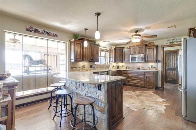 kitchen with stainless steel appliances, wood-type flooring, a center island, a textured ceiling, and decorative light fixtures