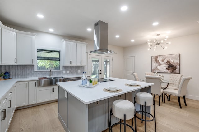 kitchen featuring tasteful backsplash, a kitchen island, white cabinetry, island range hood, and light hardwood / wood-style flooring