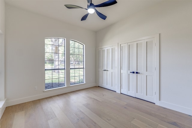 unfurnished bedroom with light hardwood / wood-style flooring, multiple windows, two closets, and ceiling fan