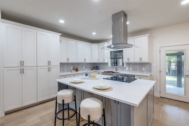 kitchen featuring white cabinets, a kitchen island, island range hood, light hardwood / wood-style flooring, and sink