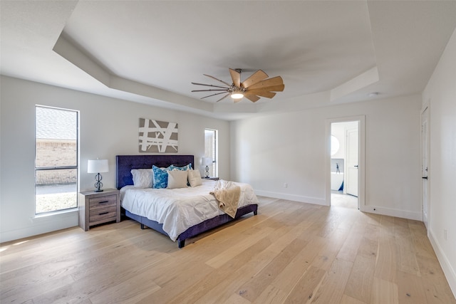 bedroom featuring connected bathroom, ceiling fan, a tray ceiling, and light hardwood / wood-style flooring