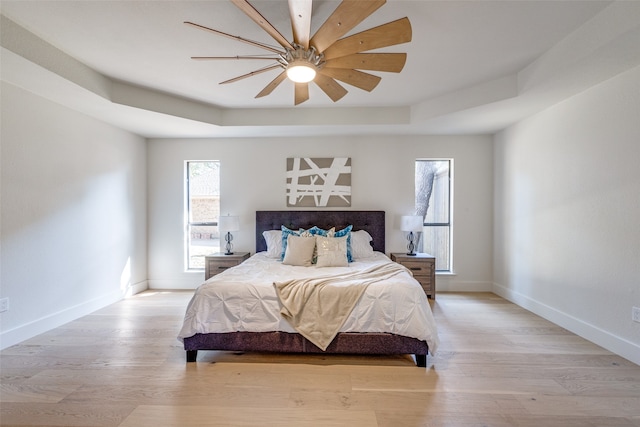 bedroom featuring a tray ceiling, light wood-type flooring, and ceiling fan