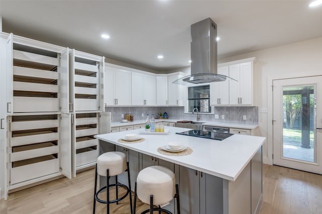 kitchen featuring island range hood, a kitchen island, sink, white cabinetry, and light hardwood / wood-style floors