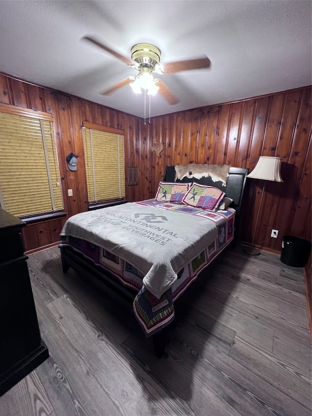 bedroom with ceiling fan, a textured ceiling, wooden walls, and hardwood / wood-style floors