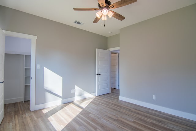 unfurnished bedroom featuring light hardwood / wood-style floors, a spacious closet, a closet, and ceiling fan