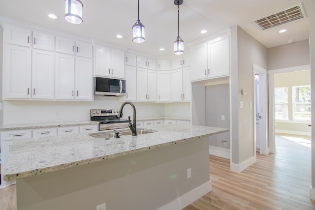 kitchen with sink, an island with sink, decorative light fixtures, and appliances with stainless steel finishes