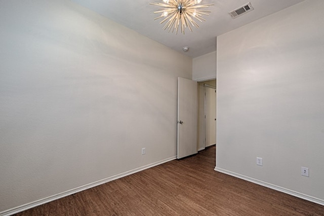 spare room featuring dark wood-type flooring and a notable chandelier