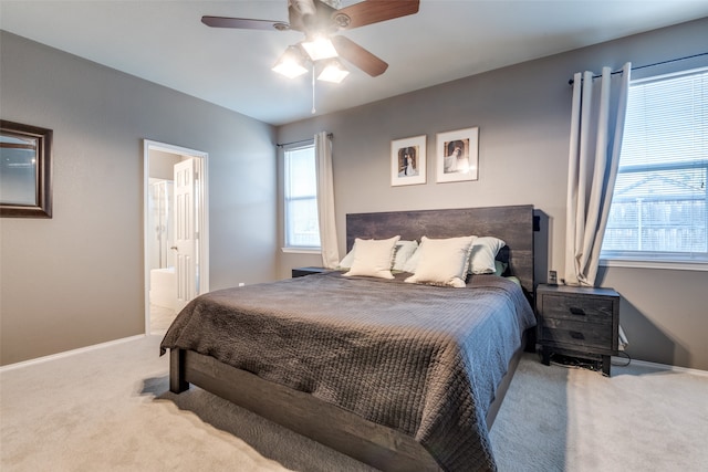 bedroom featuring connected bathroom, multiple windows, light colored carpet, and ceiling fan