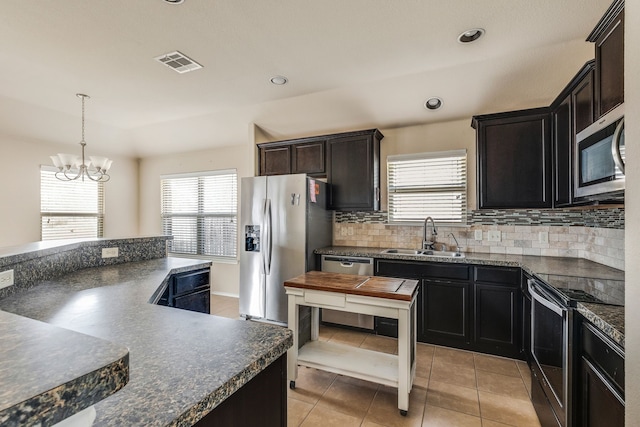 kitchen featuring decorative light fixtures, backsplash, sink, stainless steel appliances, and light tile patterned floors