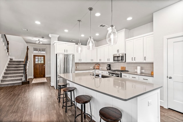 kitchen with a kitchen island with sink, sink, dark hardwood / wood-style floors, appliances with stainless steel finishes, and decorative light fixtures