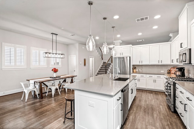 kitchen with hanging light fixtures, sink, an island with sink, appliances with stainless steel finishes, and dark hardwood / wood-style flooring