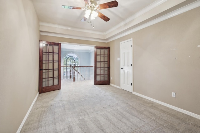 carpeted empty room with a raised ceiling, crown molding, french doors, and ceiling fan with notable chandelier