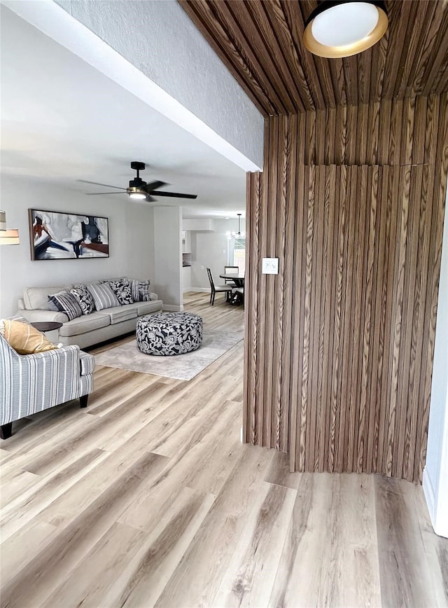 living room with wood walls, light wood-type flooring, and ceiling fan