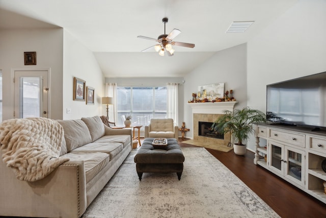 living room with ceiling fan, vaulted ceiling, a tile fireplace, and dark hardwood / wood-style floors