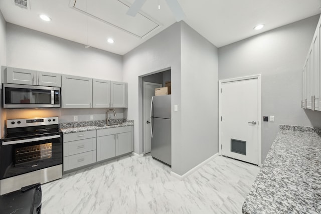 kitchen with gray cabinetry, light stone counters, appliances with stainless steel finishes, and sink