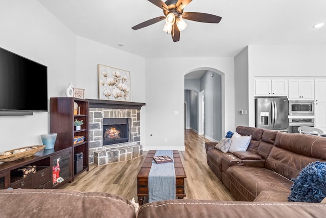 living room with a stone fireplace, ceiling fan, and light wood-type flooring