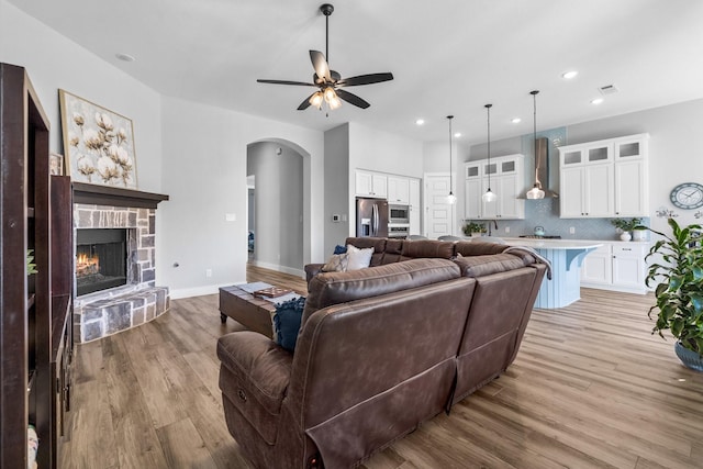 living room with ceiling fan, a stone fireplace, and light wood-type flooring