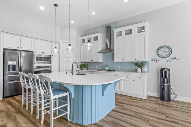 kitchen featuring wall chimney exhaust hood, sink, white cabinetry, an island with sink, and stainless steel appliances