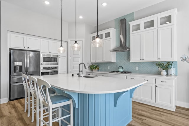 kitchen with wall chimney range hood, sink, a kitchen island with sink, white cabinetry, and stainless steel appliances