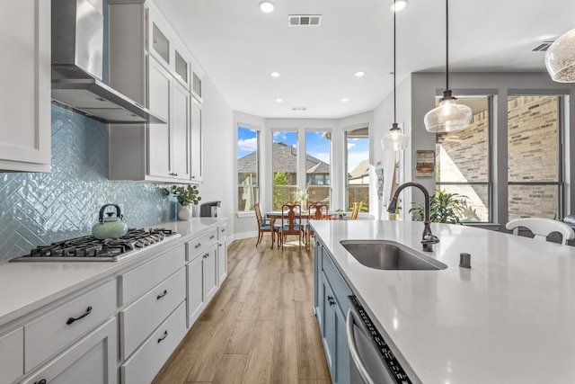 kitchen with wall chimney exhaust hood, sink, pendant lighting, stainless steel appliances, and white cabinets